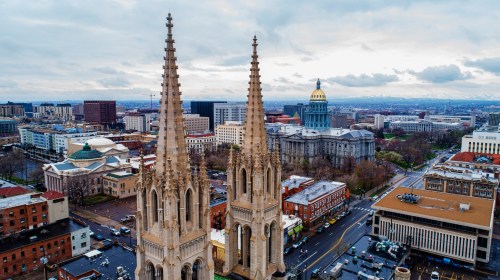 Aerial view of city skyline featuring tall church spires and a government building with a golden dome.