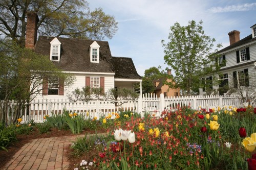 A charming white house with a sloped roof, surrounded by colorful tulips and a white picket fence.