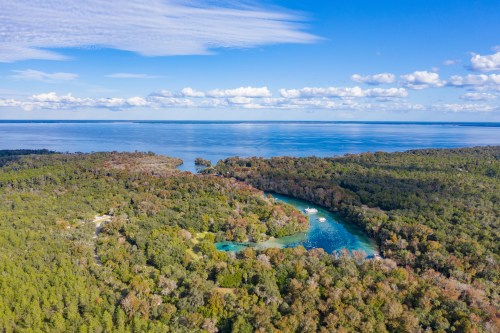 Aerial view of a lush, green landscape with a winding river and blue waters under a partly cloudy sky.