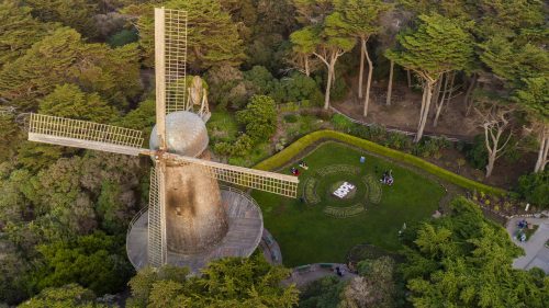 Aerial view of a historic windmill surrounded by lush greenery and a garden with people enjoying the area.