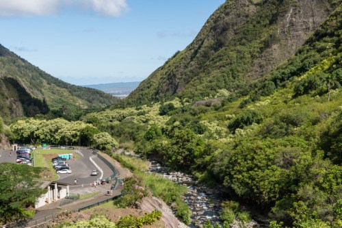 A scenic view of a lush valley with mountains, a river, and a parking area in the foreground.