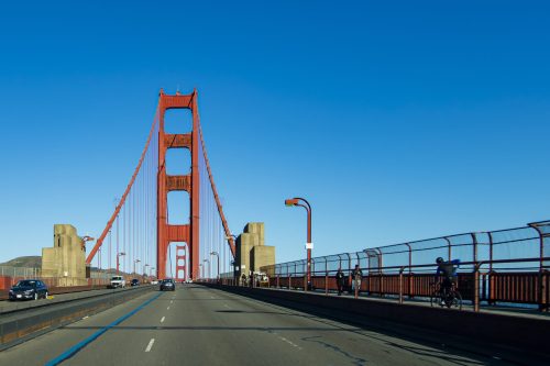 View of the Golden Gate Bridge from a roadway, with clear blue skies and vehicles passing by.
