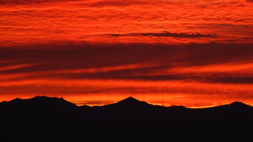 Silhouetted mountains against a vibrant red and orange sunset sky with dramatic cloud patterns.