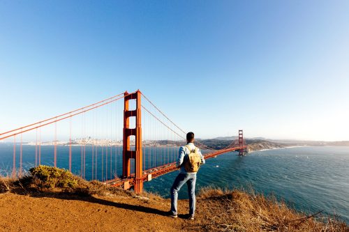 A person stands on a hillside overlooking the Golden Gate Bridge and San Francisco Bay on a clear day.