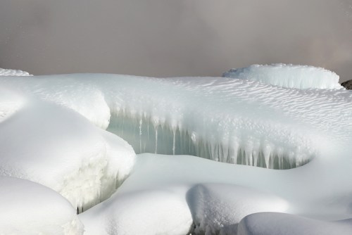 A serene winter landscape featuring icy formations and snow-covered surfaces, with icicles hanging from the edges.