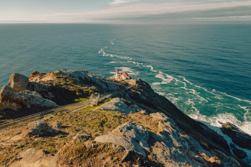 A scenic coastal view featuring a lighthouse on a rocky cliff, with waves crashing against the shore below.