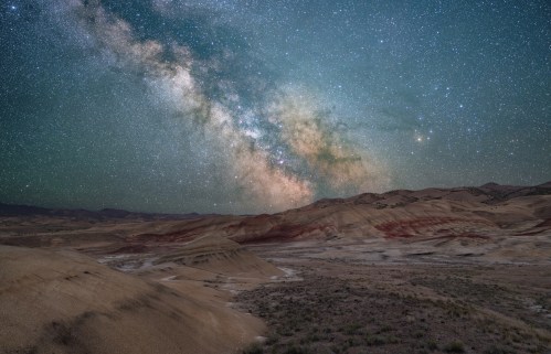 A stunning night sky filled with stars and the Milky Way over colorful, rugged desert hills.