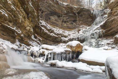 A serene winter scene featuring a waterfall cascading over rocky cliffs, surrounded by snow and icicles.