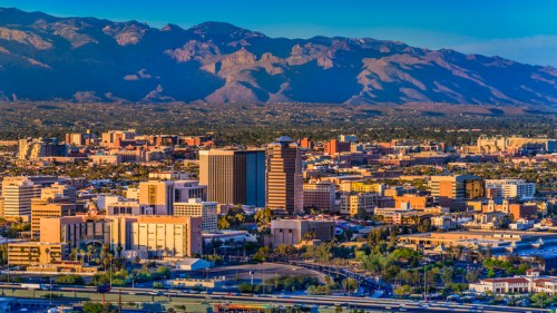 A panoramic view of a city skyline with mountains in the background, showcasing buildings and greenery.
