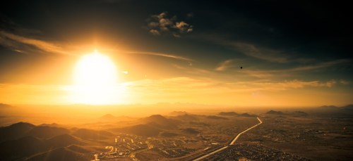 A breathtaking sunset over a mountainous landscape, with a winding road and scattered buildings below.