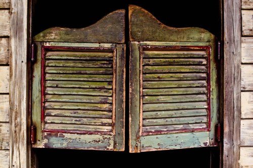 Weathered wooden shutters with green paint and slats, set against a rustic wooden wall.
