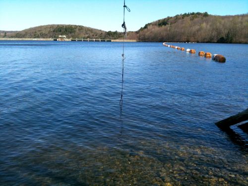 A calm lake with clear water, surrounded by hills, and a buoy line stretching across the water's surface.