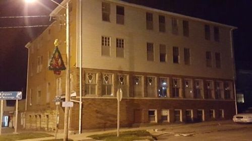 A large, three-story building at night, with windows illuminated and a decorative wreath hanging nearby.