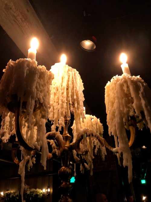 A close-up of a chandelier with three lit candles, featuring dripping white wax and a warm, dimly lit ambiance.