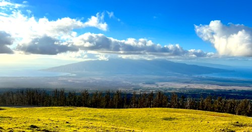 A scenic view of a lush green landscape with mountains and clouds under a bright blue sky.