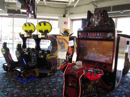 Two arcade games: one themed around Batman with seats, and another titled "Aliens Armageddon" with a large screen.