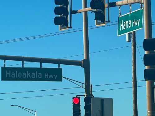 Traffic signals and street signs for Haleakala Hwy and Hana Hwy against a clear blue sky.