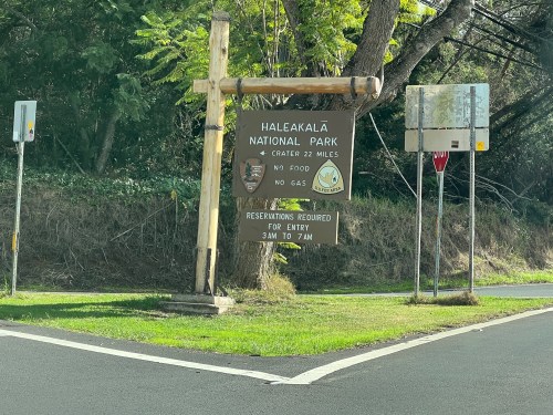 Sign for Haleakalā National Park, indicating park details and reservation requirements, surrounded by greenery.