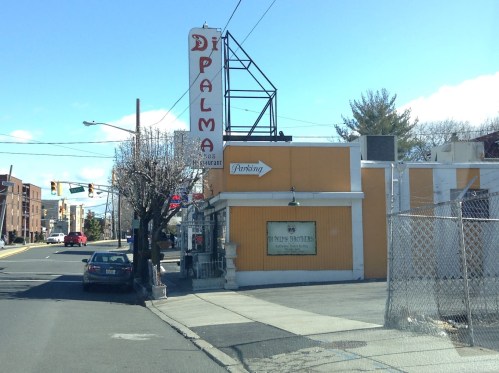 A street view of a restaurant named "D'Palma" with a parking sign, surrounded by buildings and trees.