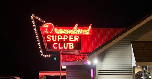 Neon sign for "Dreamland Supper Club" illuminated at night, showcasing a retro diner aesthetic.
