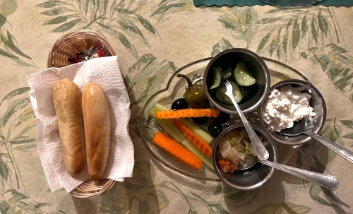A plate with assorted vegetables, cottage cheese, and a basket of two bread rolls on a leafy tablecloth.