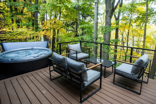 A cozy deck with a hot tub and seating area, surrounded by vibrant autumn trees.