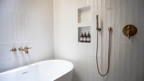 A modern bathroom featuring a freestanding white bathtub, gold fixtures, and a wall niche with bottles.