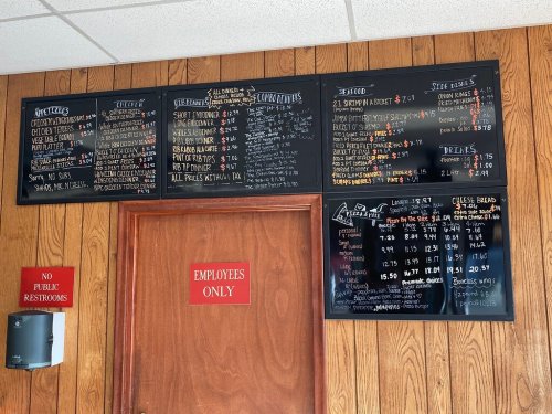 Menu board displaying appetizers, entrees, sides, and drinks, with prices listed on a black chalkboard background.