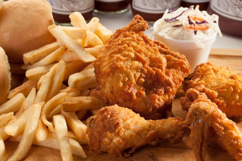 A plate of crispy fried chicken, golden French fries, a roll, and coleslaw in a cup.