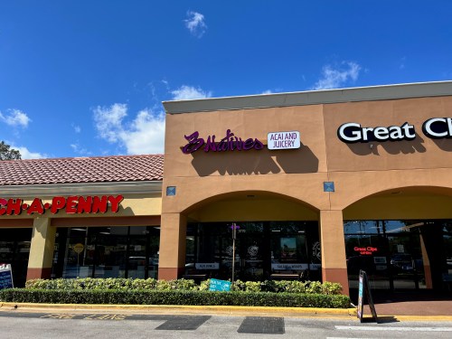 Storefront featuring "3 Natives Acai and Juicery" sign, with "Ch-A-Penny" and "Great Clips" nearby under a blue sky.