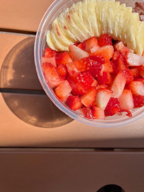 A clear container filled with diced strawberries and pineapple slices, resting on a wooden surface.