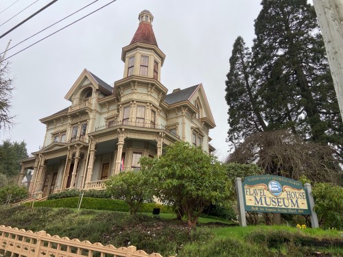 Historic Flavel House Museum, a Victorian-style mansion with a distinctive tower, surrounded by lush greenery.