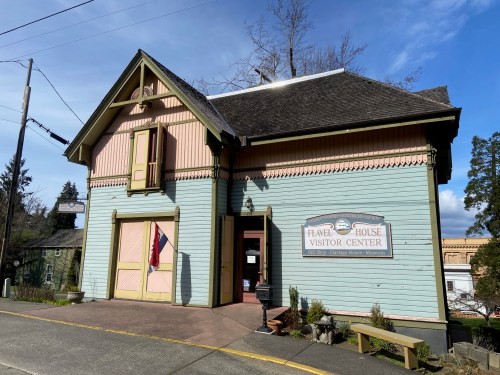 A colorful Victorian-style building with a sign reading "Flavel House Visitor Center" and a clear blue sky above.