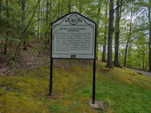 Sign detailing the Hawk's Nest Tunnel disaster, surrounded by trees in a wooded area.