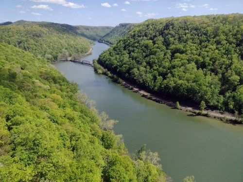 Aerial view of a winding river surrounded by lush green hills and trees under a clear blue sky.