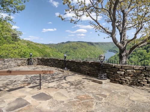 Scenic view from a stone overlook, featuring lush green hills and a river under a blue sky with scattered clouds.