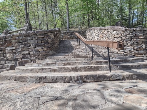 Stone steps lead upward, flanked by a rustic railing and surrounded by lush green trees.