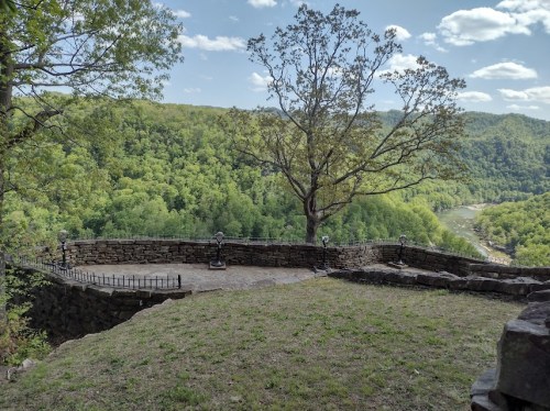 Scenic view from a stone overlook, featuring lush green hills and a river under a partly cloudy sky.