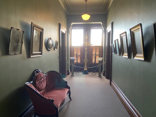 A hallway with green walls, framed artwork, a vintage sofa, and a decorative lamp at the end.