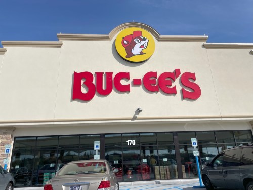 Exterior of a Buc-ee's convenience store with a large logo and bright signage, featuring parked cars in front.