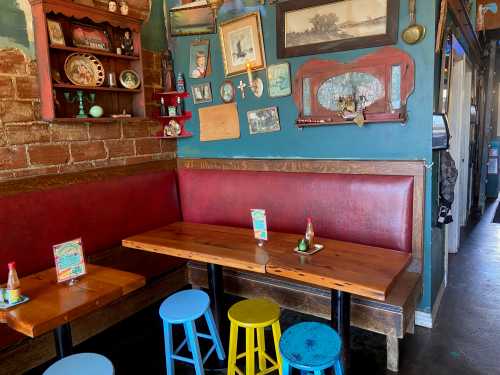 Cozy restaurant interior with a red booth, wooden tables, colorful stools, and eclectic wall decor.