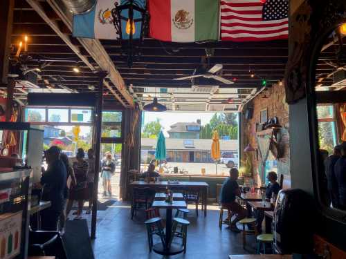 Interior of a vibrant café with flags hanging, colorful furniture, and people enjoying the space. Bright and inviting atmosphere.