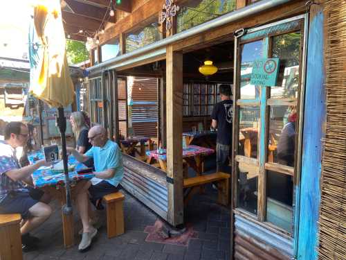 Outdoor dining area with colorful tables, people eating, and a "No Smoking" sign visible on the wall.