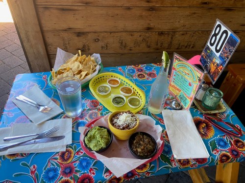 A colorful table set with chips, guacamole, a bowl of food, sauces, a drink, and a table number.