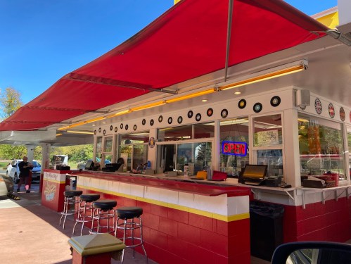 A retro-style diner with red awnings, vinyl records on the walls, and an "OPEN" sign, set against a clear blue sky.