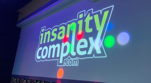 Logo of "insanitycomplex.com" projected on a wall with colorful light spots.