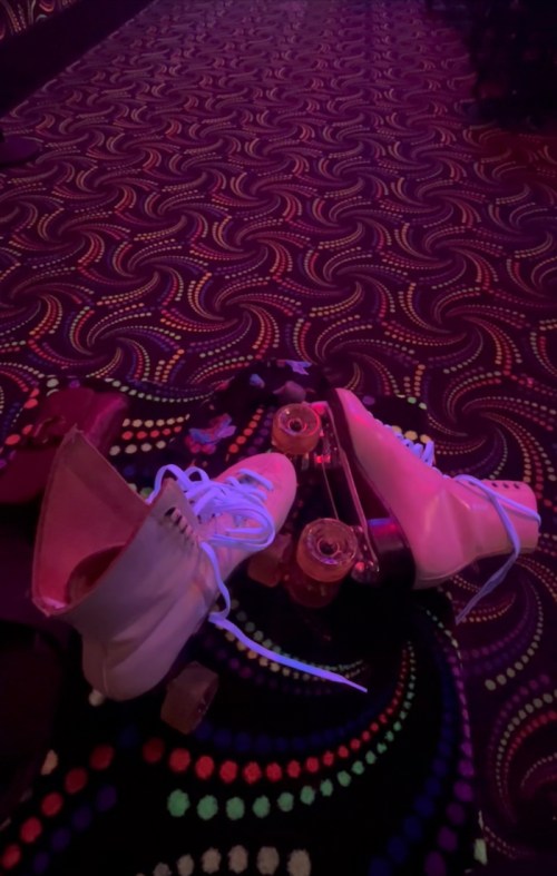 A pair of white roller skates resting on a colorful, patterned floor in a skating rink.
