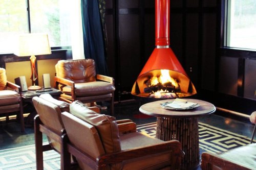 Cozy living room with a modern orange fireplace, wooden chairs, and a round table, creating a warm atmosphere.