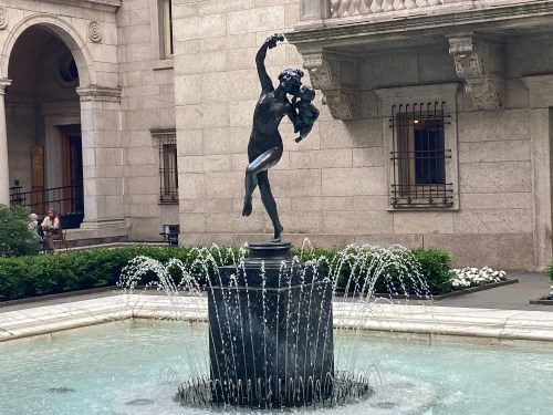 A graceful statue of a woman holding a child, surrounded by a fountain in a courtyard.