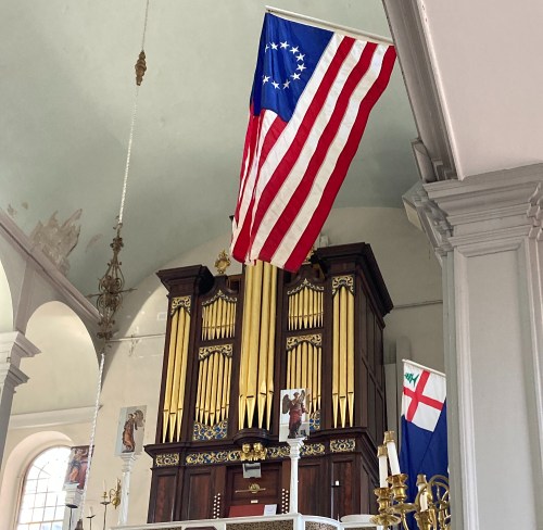 Interior of a church featuring a large organ and a historic American flag hanging from the ceiling.